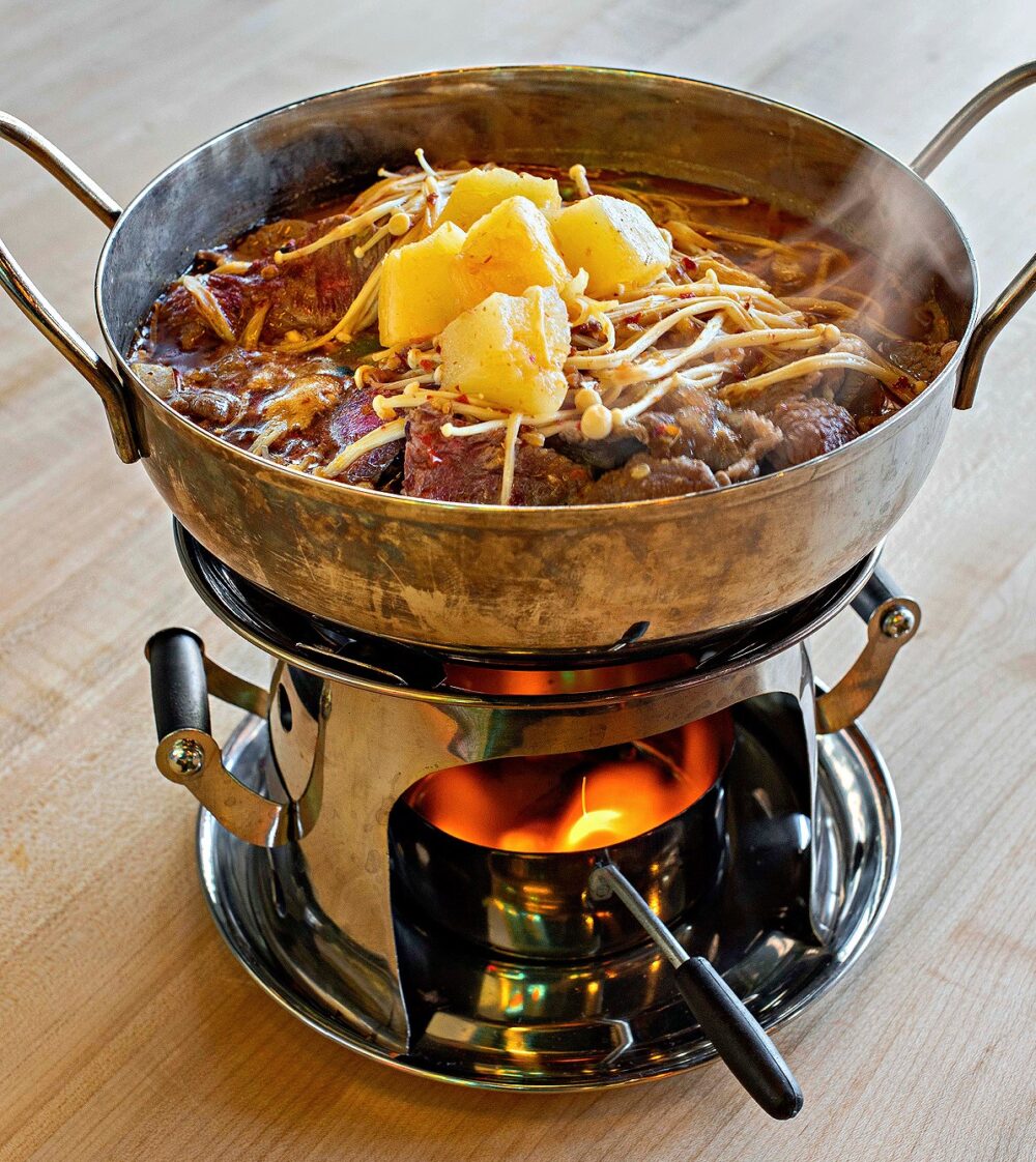 Satay Wagyu Beef Casserole: featuring sliced Wagyu beef with peanut satay sauce, enoki mushrooms, vermicelli, and pineapple. $19.95. One of three Hong Kong inspired casseroles, each presented under a flickering open flame. for Celebrate Lunar New Year Hong Kong Style at Ken Kee